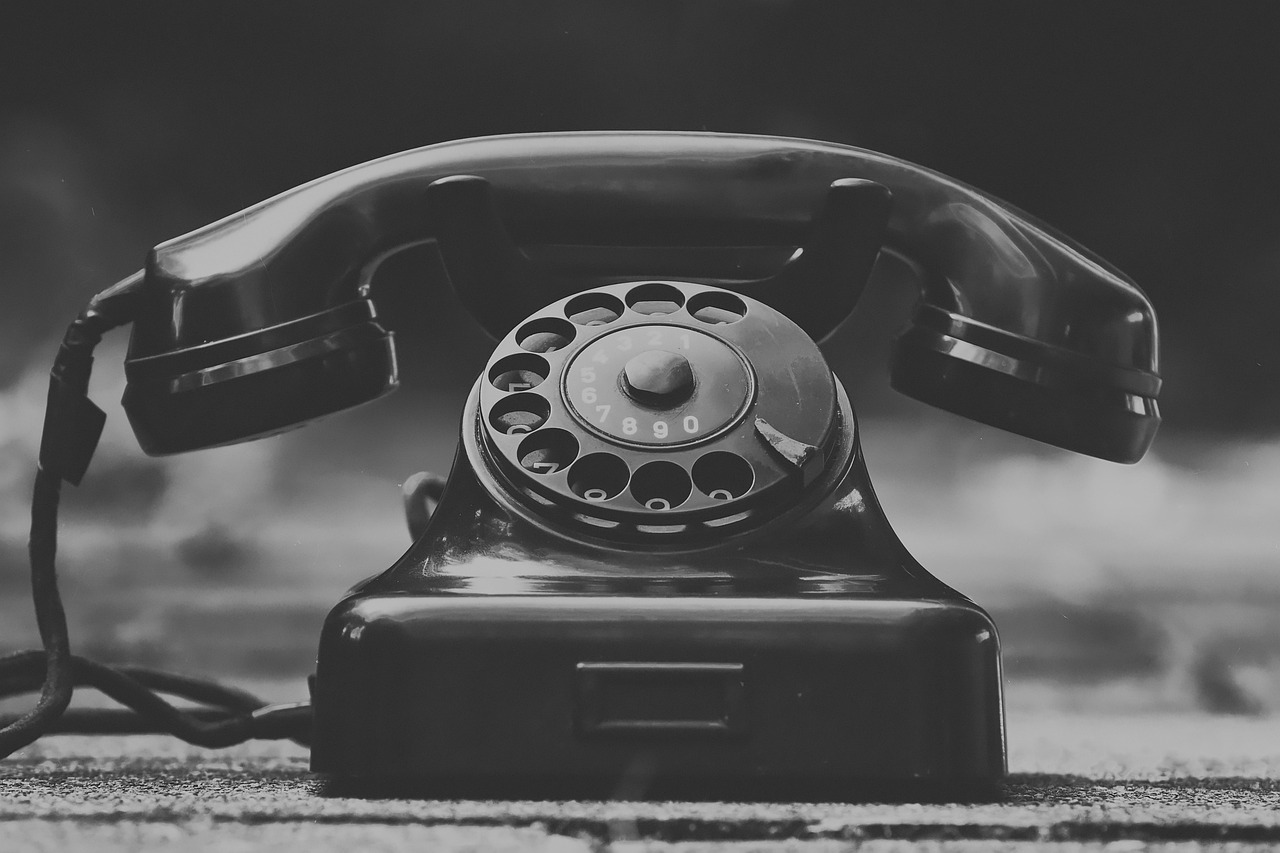 Schwarz-weiße Nahaufnahme eines alten Wählscheibentelefons mit aufgelegtem Hörer