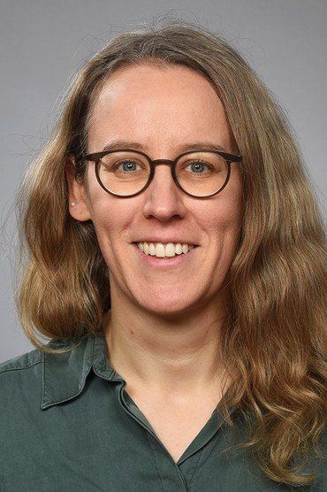 Pfarrerin Ilka Wehrend mit schulterlangem, welligem, hellbraunem Haar trägt ein dunkelgrünes Hemd mit offenem Kragen.