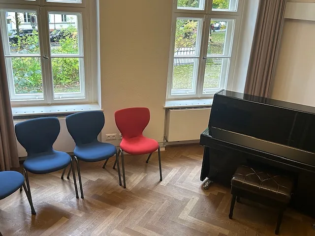 Kinderchorprobe mit Klavier und zwei blauen und einem roten Stuhl.