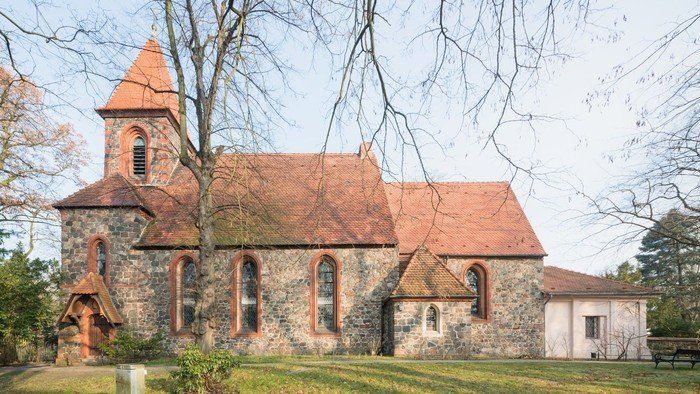 Kirche Britz Dorf mit rotem Ziegeldach, Feldsteinmauerwerk und Spitzbogenfenstern, umgeben von Bäumen und einer Bank