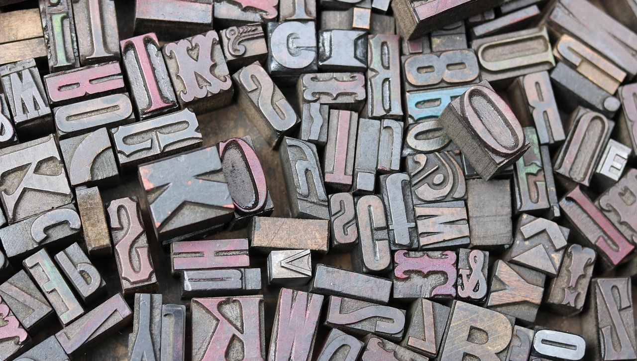 Zahlreiche Metallbuchstaben und -zeichen in verschiedenen Größen und Schriftarten, teils mit verblasster blauer und roter Farbe.