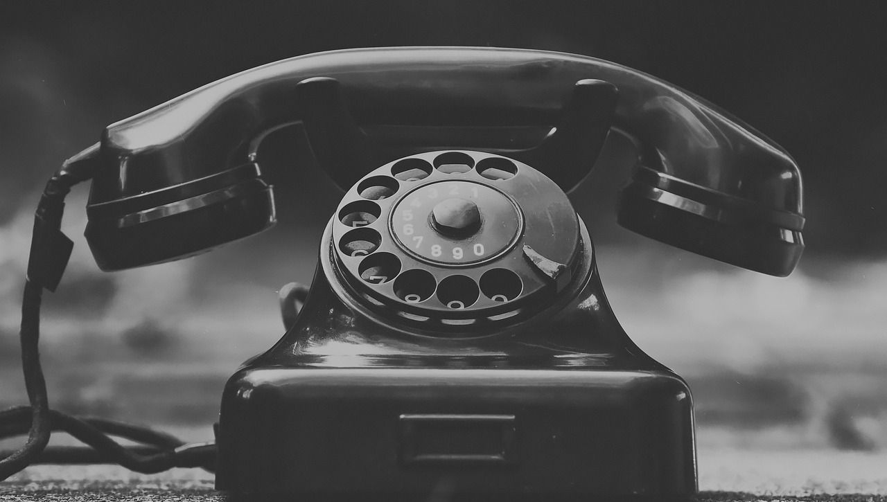 Schwarz-weiße Nahaufnahme eines alten Wählscheibentelefons mit aufgelegtem Hörer