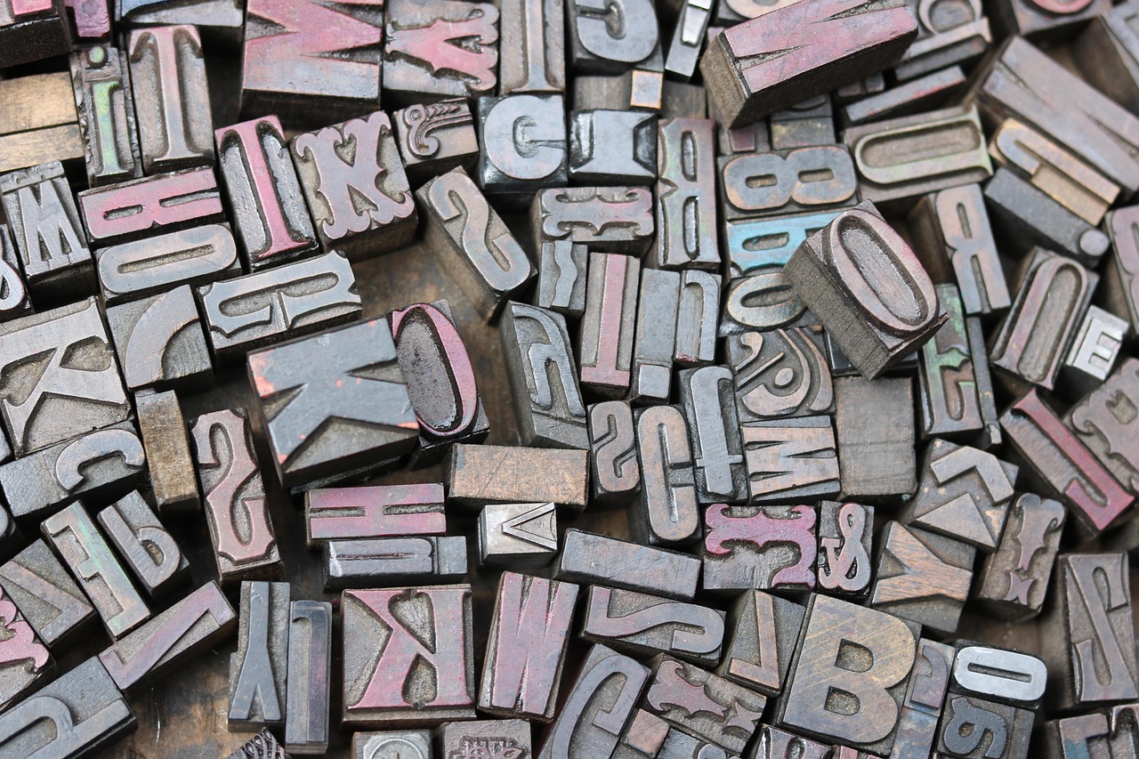Zahlreiche Metallbuchstaben und -zeichen in verschiedenen Größen und Schriftarten, teils mit verblasster blauer und roter Farbe.