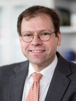 Pastor Meissner in dunklem Anzug, weißem Hemd und hellroter Krawatte vor unscharfem Hintergrund